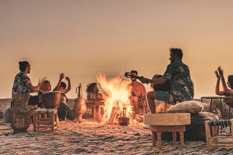Gäste mit Trommeln und Gitarre am Lagerfeuer in der Agafay-Wüste in der Dämmerung