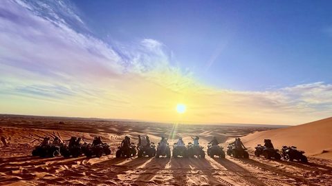 Gruppe auf Quads mit Blick auf die untergehende Sonne in den Dünen