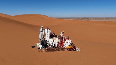 Reisende in traditioneller Kleidung auf einem Teppich in den Dünen
