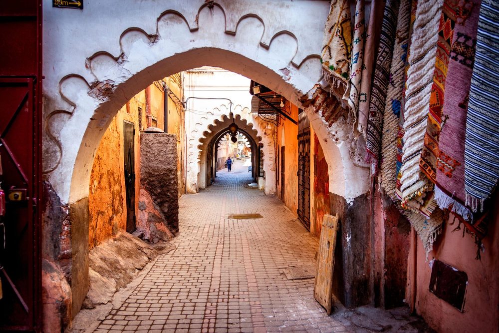 Medina lane in Marrakech with white arches and hanging rugs