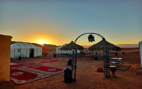 Weißes Zeltcamp bei Sonnenuntergang mit roten Teppichen und Laternen